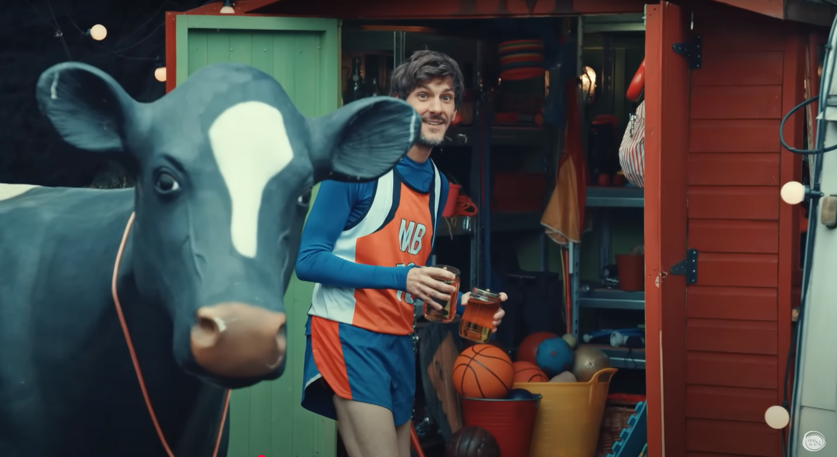 Matthew Baynton holding two jars of vinegar, standing behind a cow statue in front of a shed.