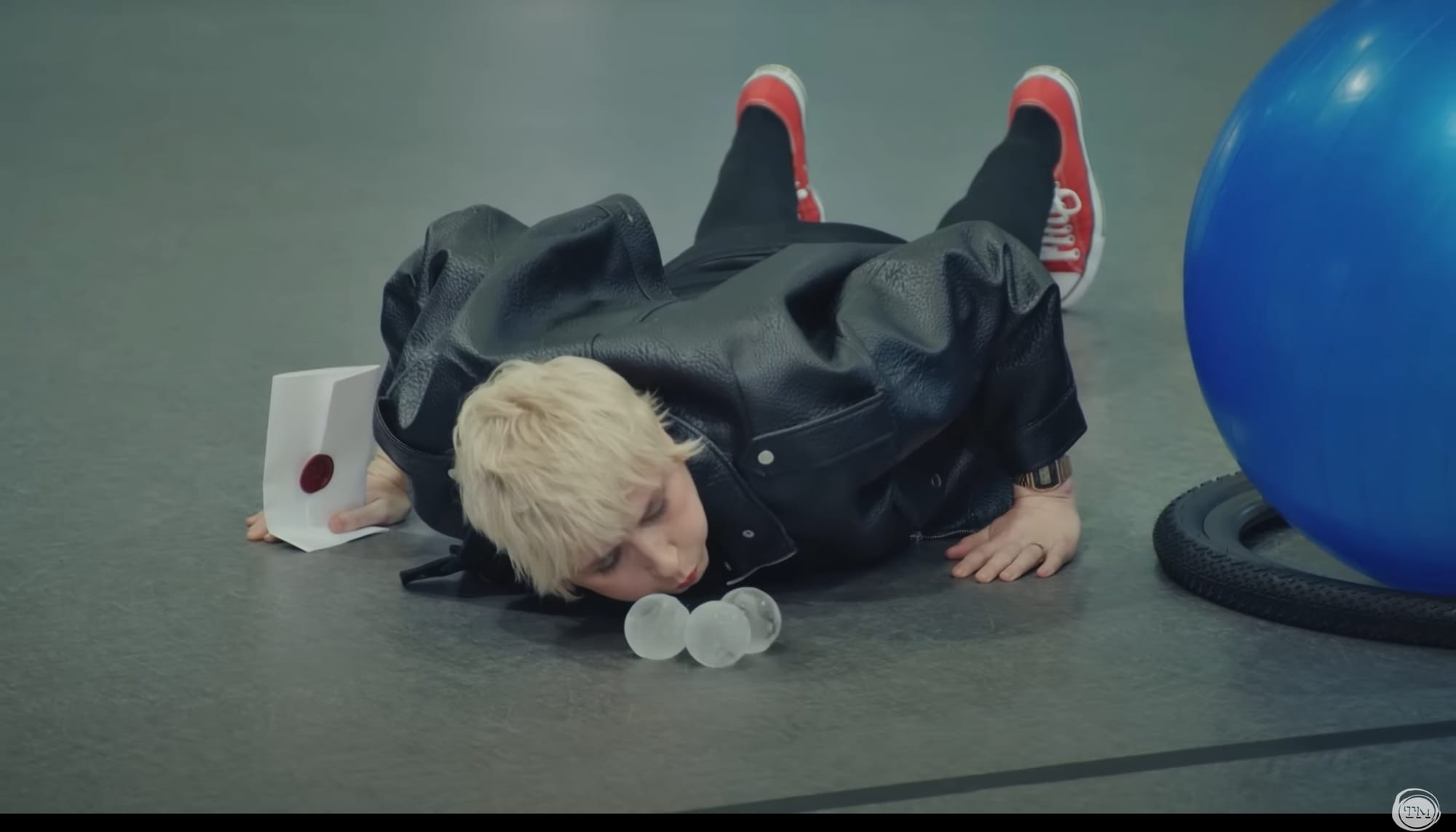 Maisie Adam lies stomach-down on the ground and blows on large round ice cubes.