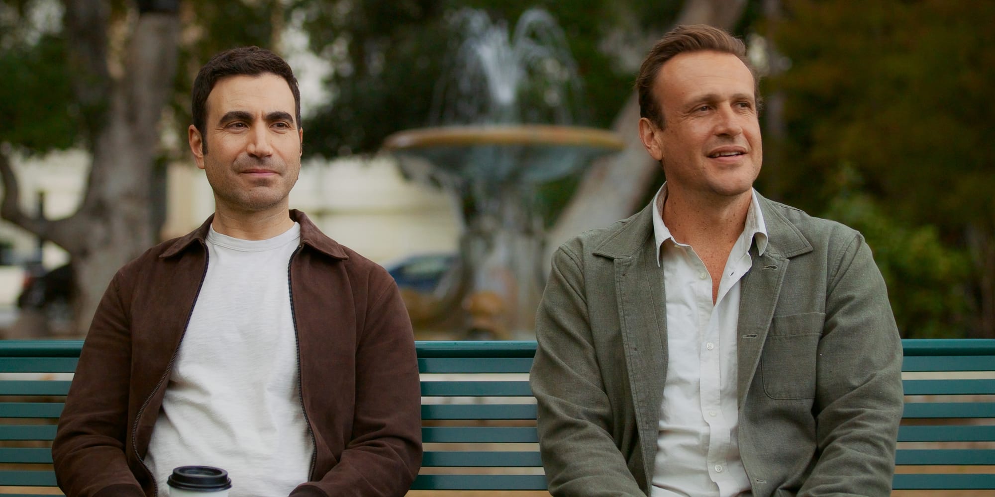 Brett Goldstein and Jason Segel sit on a park bench.